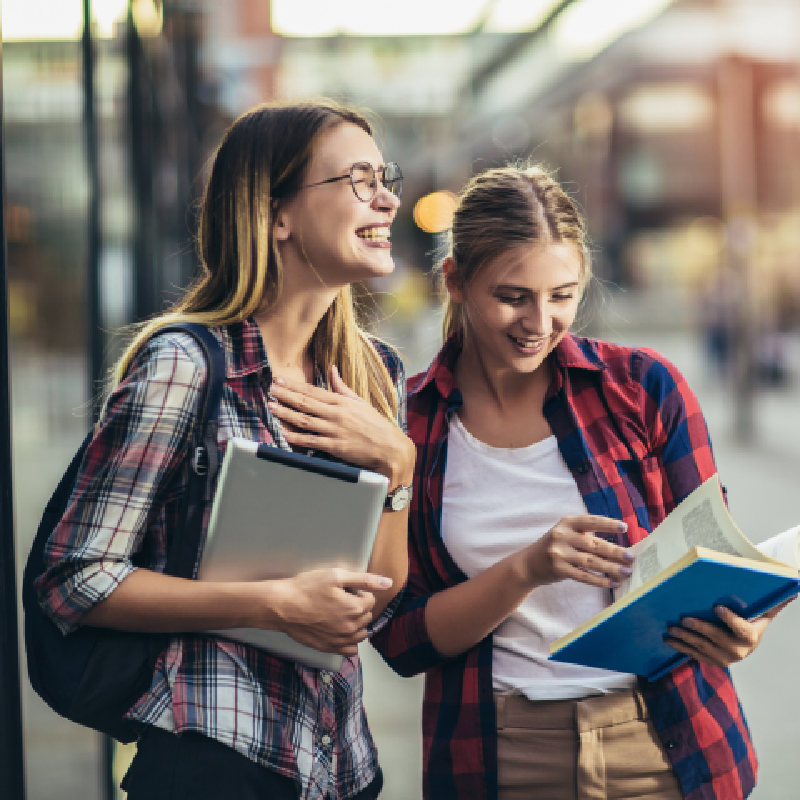 Two girls smiling looking at their education text books