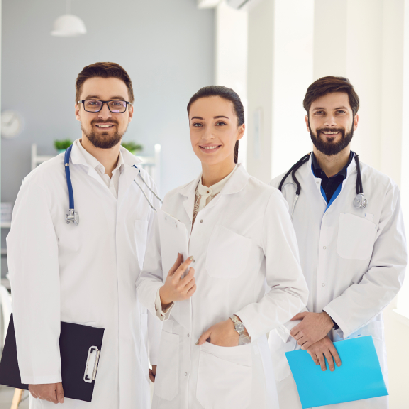Three medical care workers smiling at the camera, all wearing white doctor coats